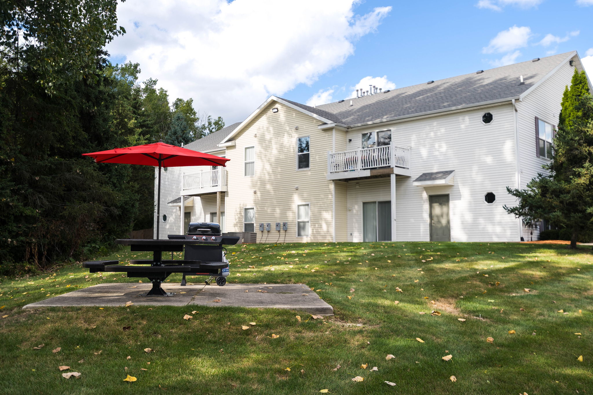 A white house with a red umbrella and a picnic table in front.
